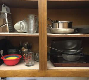 A ready to use cupboard, with a few small pans, bowls, measuring cups and hand chopper